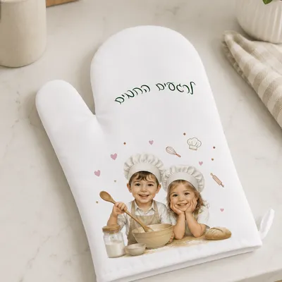כפפת תנור לבנה עם הדפס של שני ילדים בכובעי שף מחייכים, מונחת על שיש מטבח בהיר