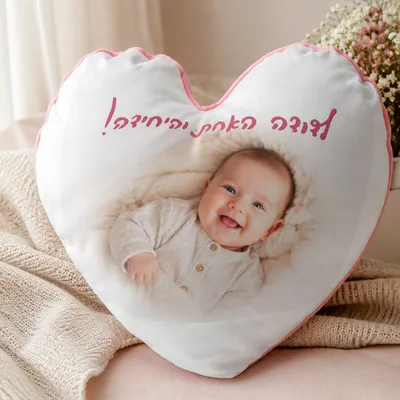 כרית בצורת לב עם הדפסת תמונת תינוק מחייך וכיתוב אישי בורוד, מונחת על מצעים בגוונים עדינים